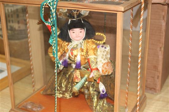 A Japanese wooden cased model of a Samurai warrior holding aloft a fan, with ornate silkwork robes, overall height 35cm, width 33cm